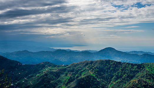 mountains covered with trees under gray clouds at daytime