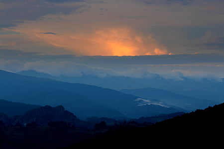 silhouette of mountain under cloudy sky at sunset