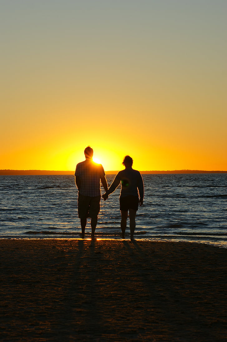 couple holding hands near beach during golden hour