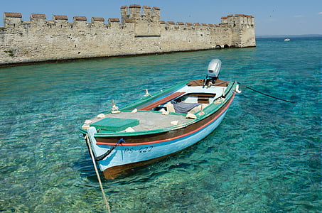 blue and brown outboard boat near brown concrete castle