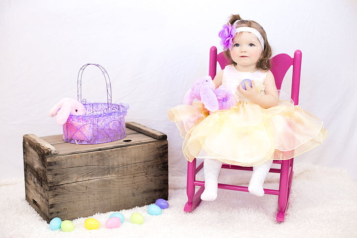 girl doll sitting on pink rocking armchair beside the brown wooden box