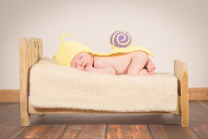 baby wearing yellow hat lying on sofa