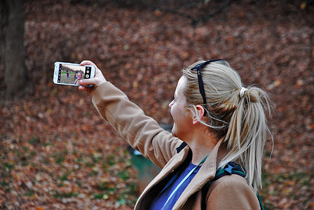 photo of a woman wearing brown jacket holding white Android smartphone