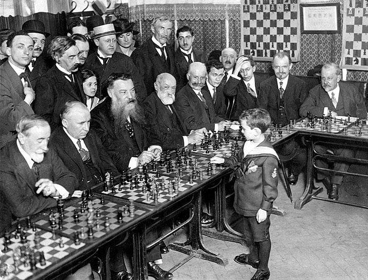 grayscale photo of group of men vs boy playing chess game