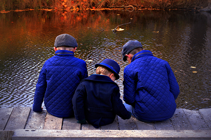 three boys sitting on boardwalk during daytime