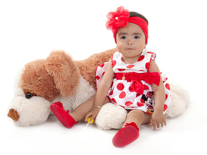 baby wearing white and red polka-dot dress beside dog plush toy