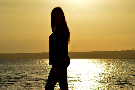 silhouette of woman standing in front of body of water