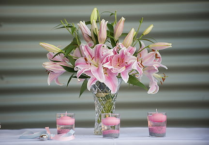 pink petaled flowers in clear vase beside three candle holders