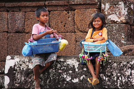 two boy and girl sitting on a concrete wall while carrying basket of goods