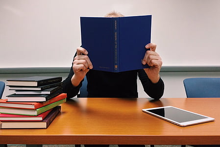 person holding blue book sitting infront of brown wooden table