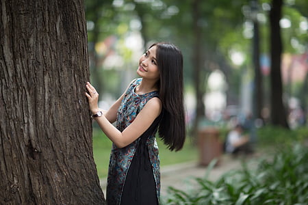 woman in black sleeveless dress touching tree