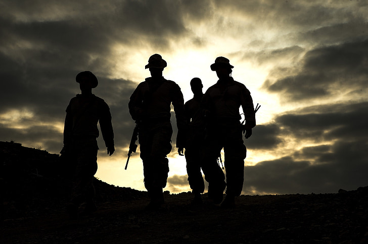 silhouette photo of four man walking on pathway carrying weapons