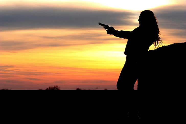 silhouette of girl holding revolver gun during golden hour