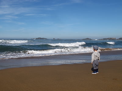 toddler wearing gray hoodie facing beach wave