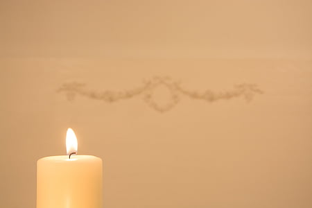 lighted white pillar candle near wall with hanged decor