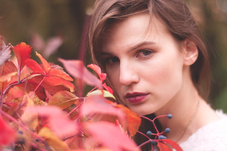 closeup photography of woman facing red leaf plant