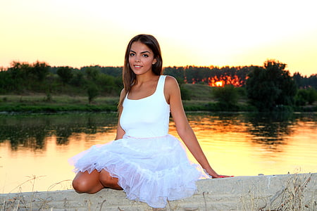 woman wearing white sleeveless dress sitting beside a lake at daytime
