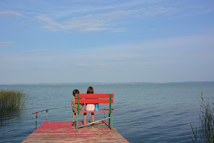 two children sitting on red and green wooden bench on bridge
