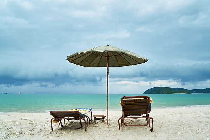 gray parasol near two sun loungers in shoreline near body of water