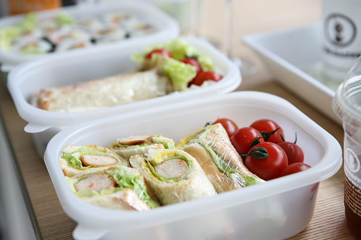 two white plastic containers with sandwich and tomatoes
