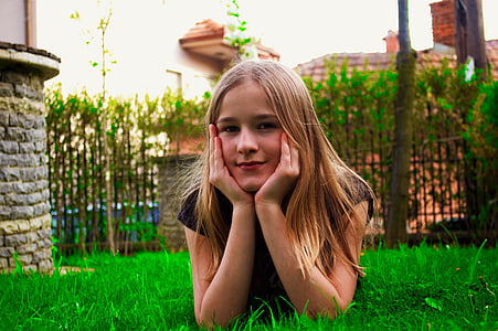 girl with blonde hair lying on grass with chin on both hands