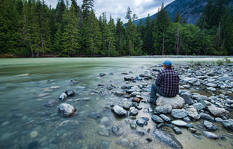 man sitting on rock near body of water