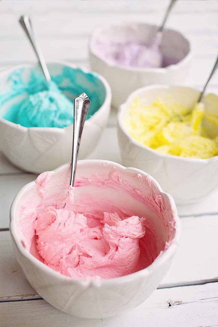 pink, purple, teal, and yellow ice creams on white ceramic bowls with four stianless steel spoons