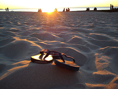 pair of flip-flops on beach sand during sunset