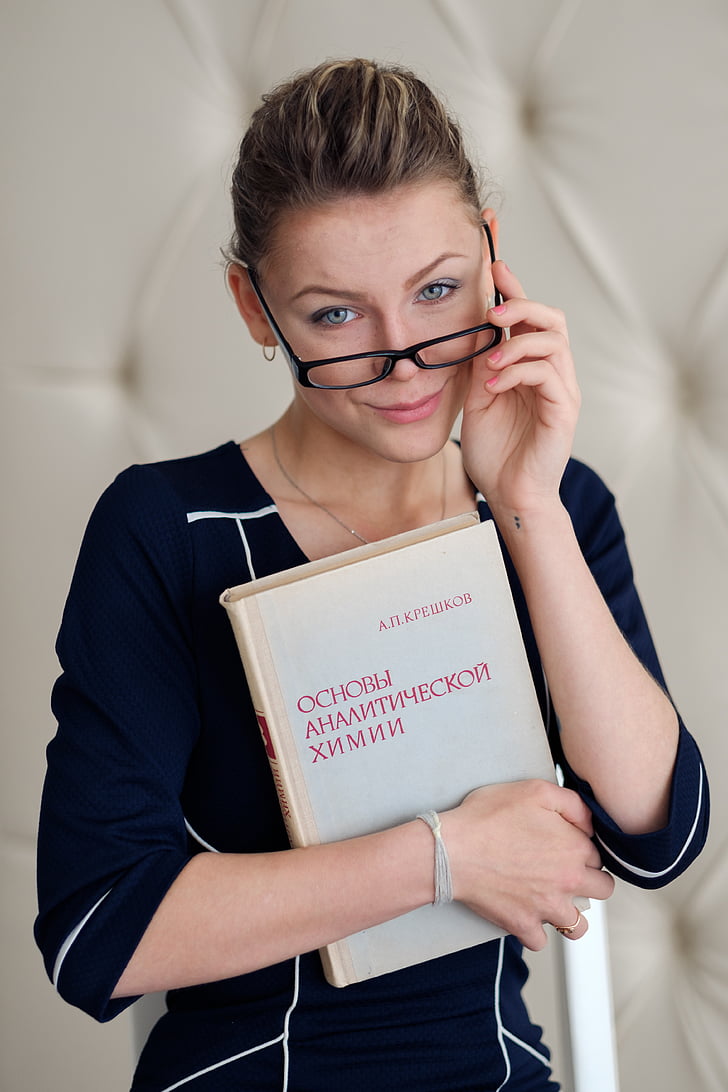 woman holding eyeglasses and white book