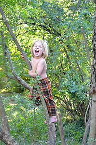 topless boy climbing small tree inside forest during daytime