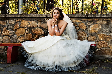 woman in wedding dress sitting on red bench during daytime