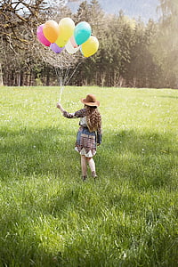 girl with brown hat holding bunch of balloons