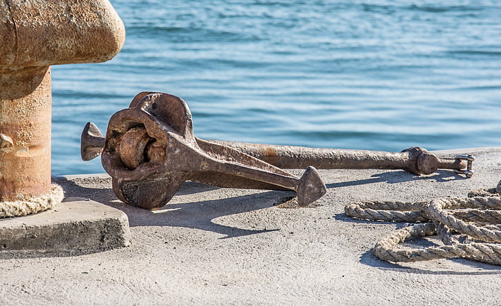 brown metal anchor on gray concrete dock near body of water