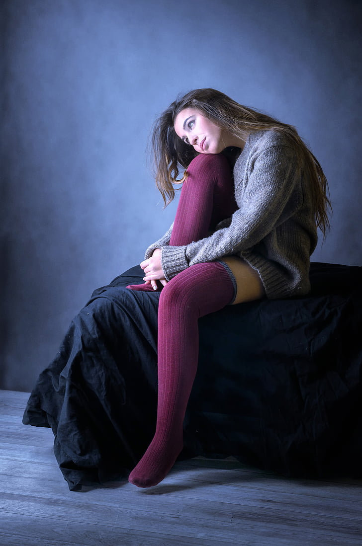 woman wearing gray sweater and pair of purple socks sitting on black mattress