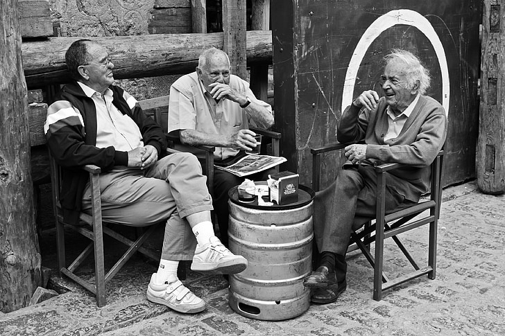 grayscale photography of three men sitting on chair while talking to each other