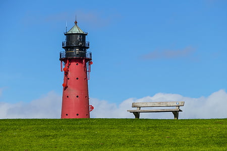 red and black lighthouse near on gray bench on grass field
