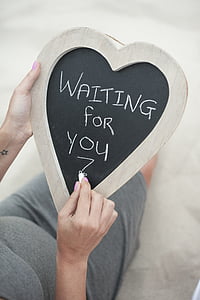 person writing a waiting for you in heart-shaped board