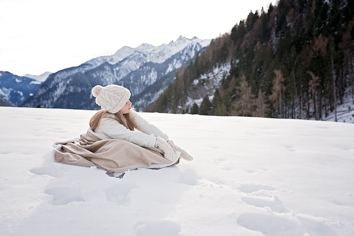 girl wearing winter coat sitting on snow field