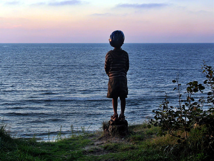 boy standing on cliff overlooking sea during daytime