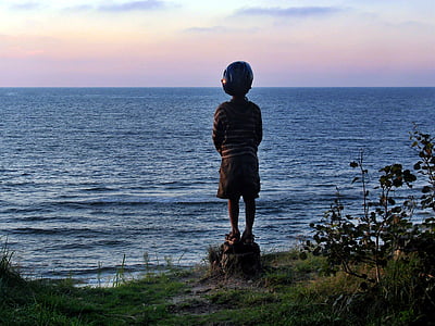 boy standing on cliff overlooking sea during daytime