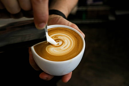 person holding white ceramic mug pouring latte art