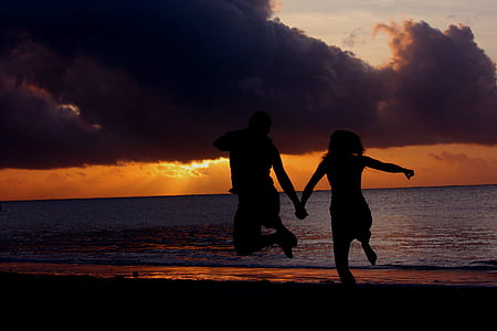 silhouette photo of two person's jumping in front of body of water