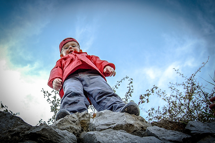boy wearing gray pants standing on rock boulder