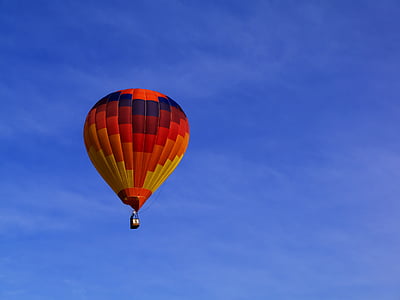 red, orange, and yellow hot air balloon floating midair under clear blue sky