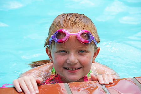 brown haired girl on body of water wearing pink goggles