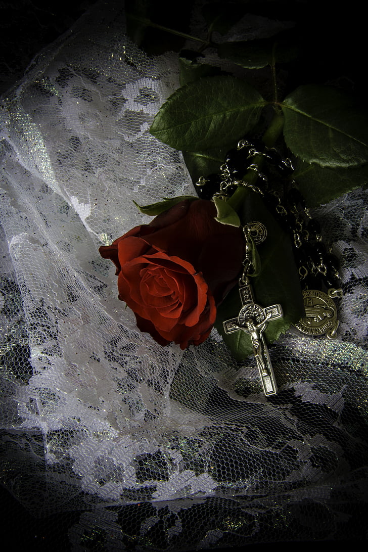 red rose beside silver-colored rosary on white lace textile
