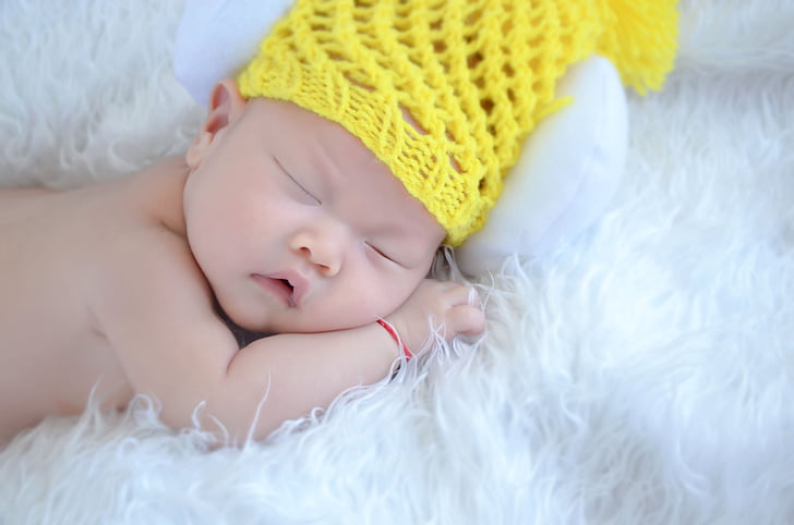 sleeping baby wearing yellow knit cap laying on white fleece textile