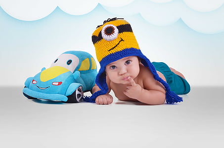 baby lying beside blue car plush toy