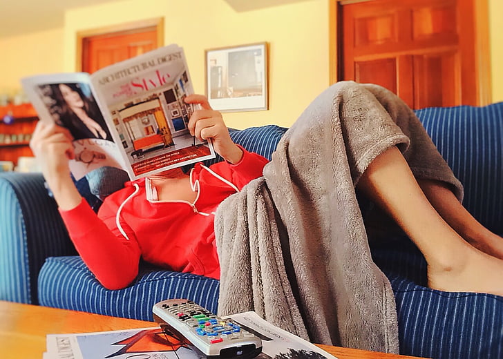 woman reading magazine lying on sofa