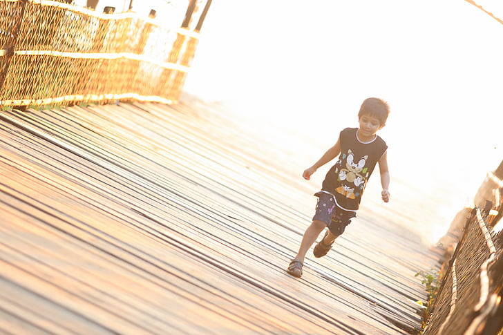 boy wearing black sonic printed tank top running on brown wooden bridge